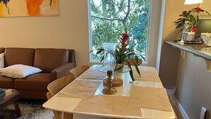 Un comedor con una mesa y sillas de madera, un florero con flores y vistas a árboles a través de una ventana.