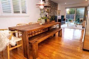 A dining area with a wooden table, benches, and chairs. There is a stone wall and a large window with blinds.