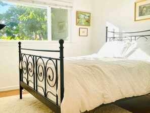 A bedroom with a metal bed frame, a window, and two framed pictures on the wall.