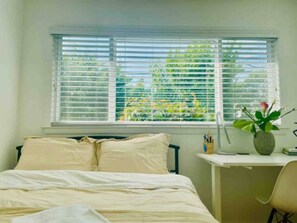 A bedroom with a bed, a desk, and a window with blinds.