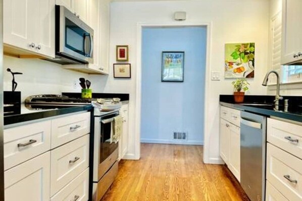 A kitchen with white cabinets, a microwave, and a stove. There is a door with a framed picture on the wall.