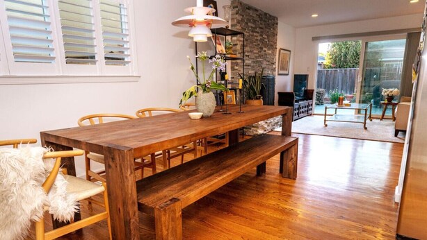 Una mesa de comedor de madera con bancos, un muro de piedra y vistas al patio trasero.