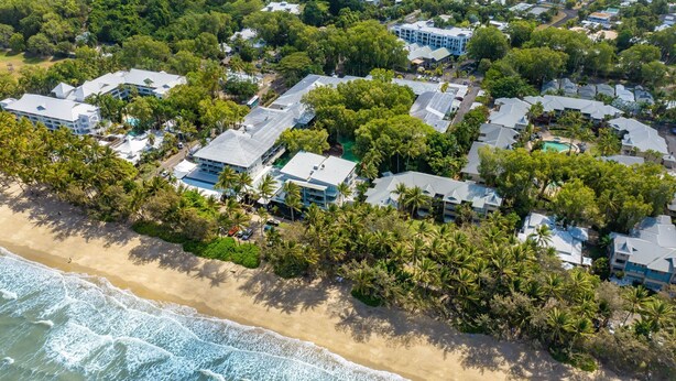 Luchtbeeld van een kustgebied met woonhuizen, omringd door weelderige palmbomen en een strand.