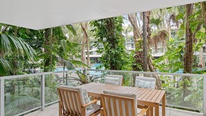 Een balkon met houten meubels, uitzicht op een zwembad en weelderige beplanting.
