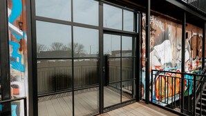 A modern building entrance with large glass doors, a wooden deck, and a mural with graffiti. - Walk To Intrust Arena - Modern Boxcar experience! (Wichita)