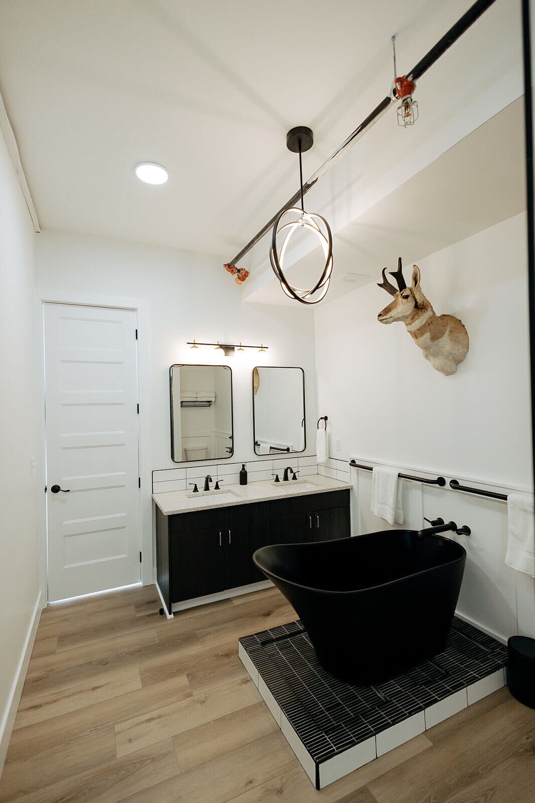 Une salle de bain moderne avec une baignoire noire, une porte blanche et une tête d’animal fixée au mur.