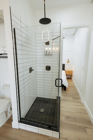 A modern shower with a glass door, white tiled walls, and a wooden floor. - Walk To Intrust Arena - Modern Boxcar experience! (Wichita)