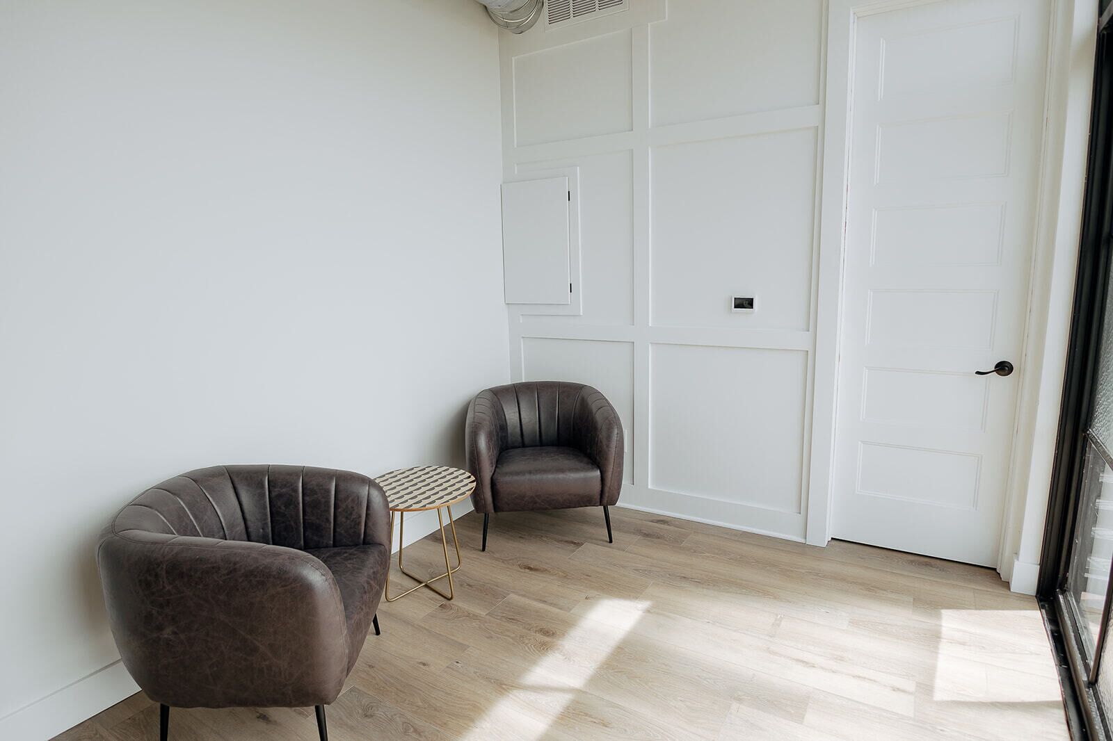 Une pièce avec deux fauteuils en cuir, une petite table ronde et une porte blanche.