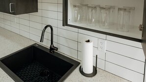 A kitchen with dark wooden cabinets, a black sink, and a white tiled backsplash. - Walk To Intrust Arena - Modern Boxcar experience! (Wichita)