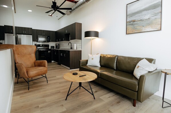 A modern living room with a leather sofa, a brown armchair, and a round coffee table. - Walk To Intrust Arena - Modern Boxcar experience! (Wichita)