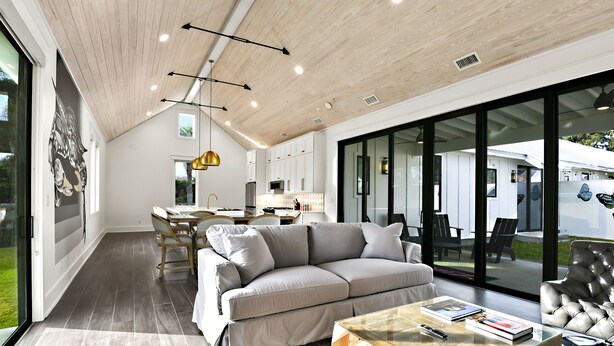 Una sala de estar moderna con un sofá gris, una mesa de centro de vidrio y una zona de comedor con una mesa y sillas blancas.
