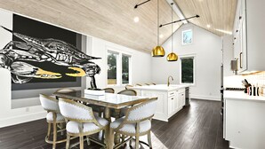 Una cocina moderna con zona de comedor, que cuenta con una isla grande, iluminación colgante y una obra de arte en la pared.