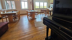 Amplia sala de estar con un piano, mesa de comedor de madera, sillas y ventanas grandes.