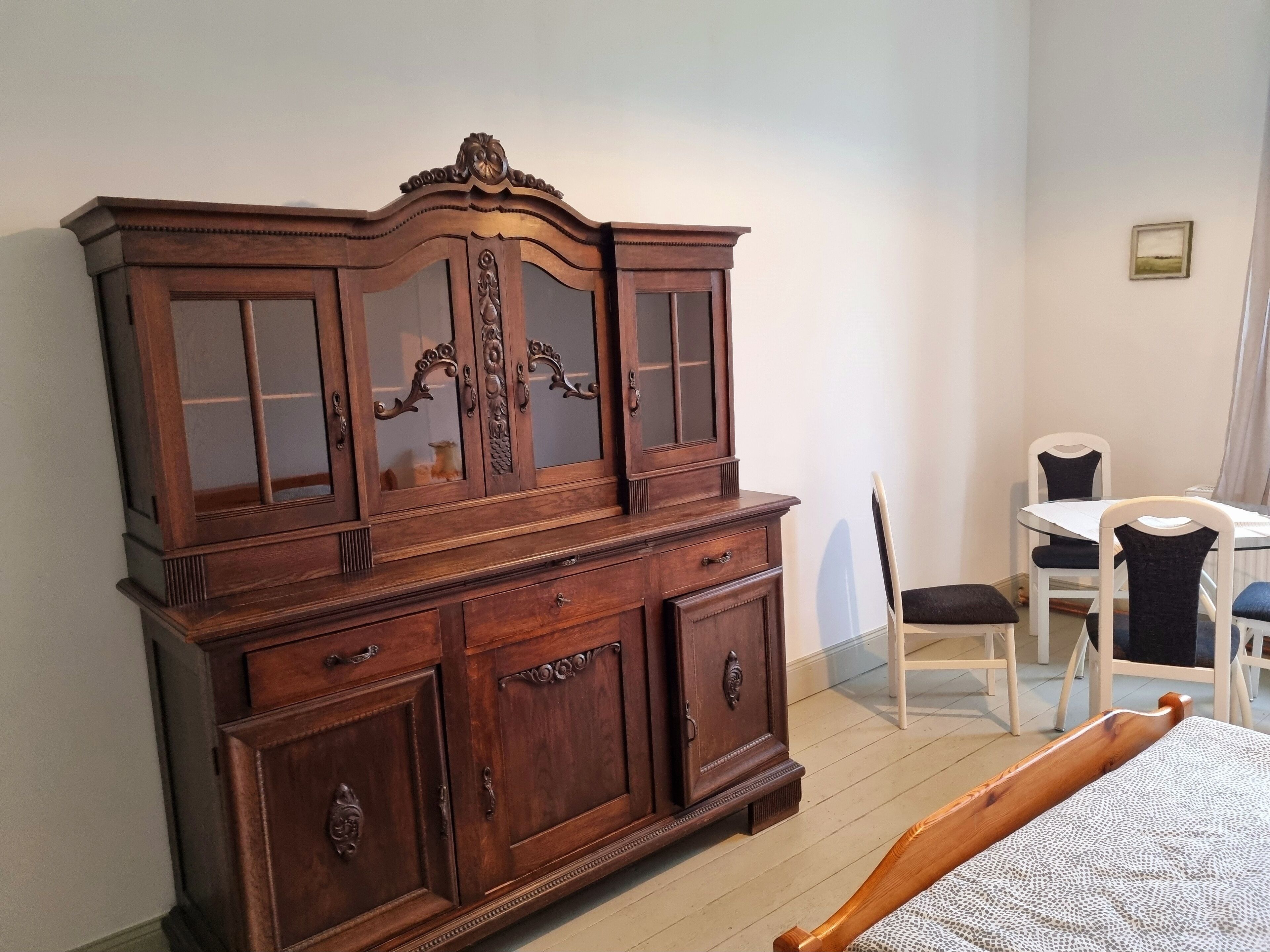 Ein Zimmer mit einem großen Holzschrank, einem Esstisch mit Stühlen und einem Bett.