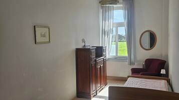 Een kamer met twee bedden, een houten kast, een spiegel en een raam met gordijnen.