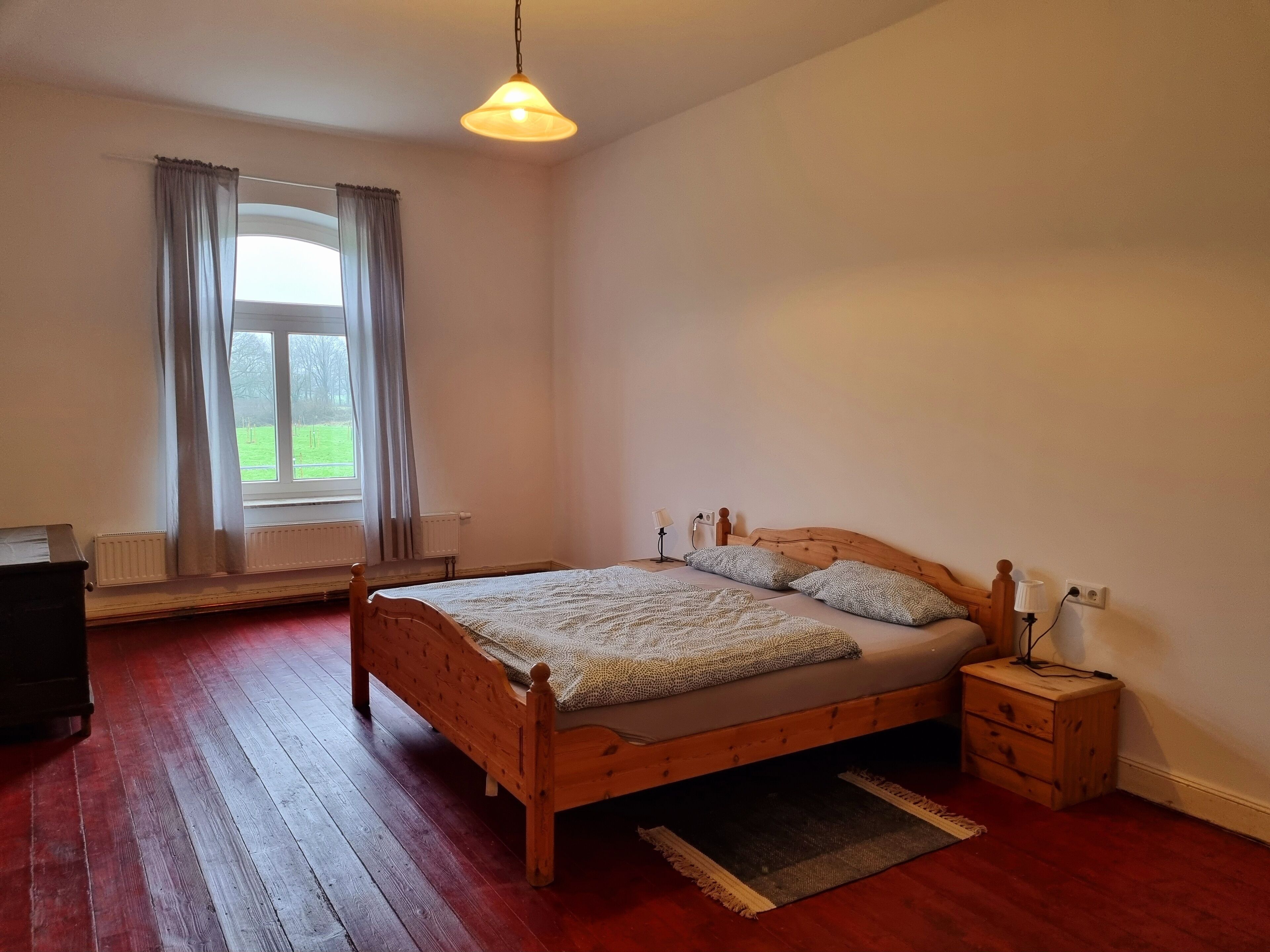 Un dormitorio con una cama de madera, una mesita de noche, una lámpara y una ventana con cortinas.