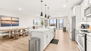 Una cucina moderna con mobili bianchi, elettrodomestici in acciaio inossidabile e luci a sospensione.