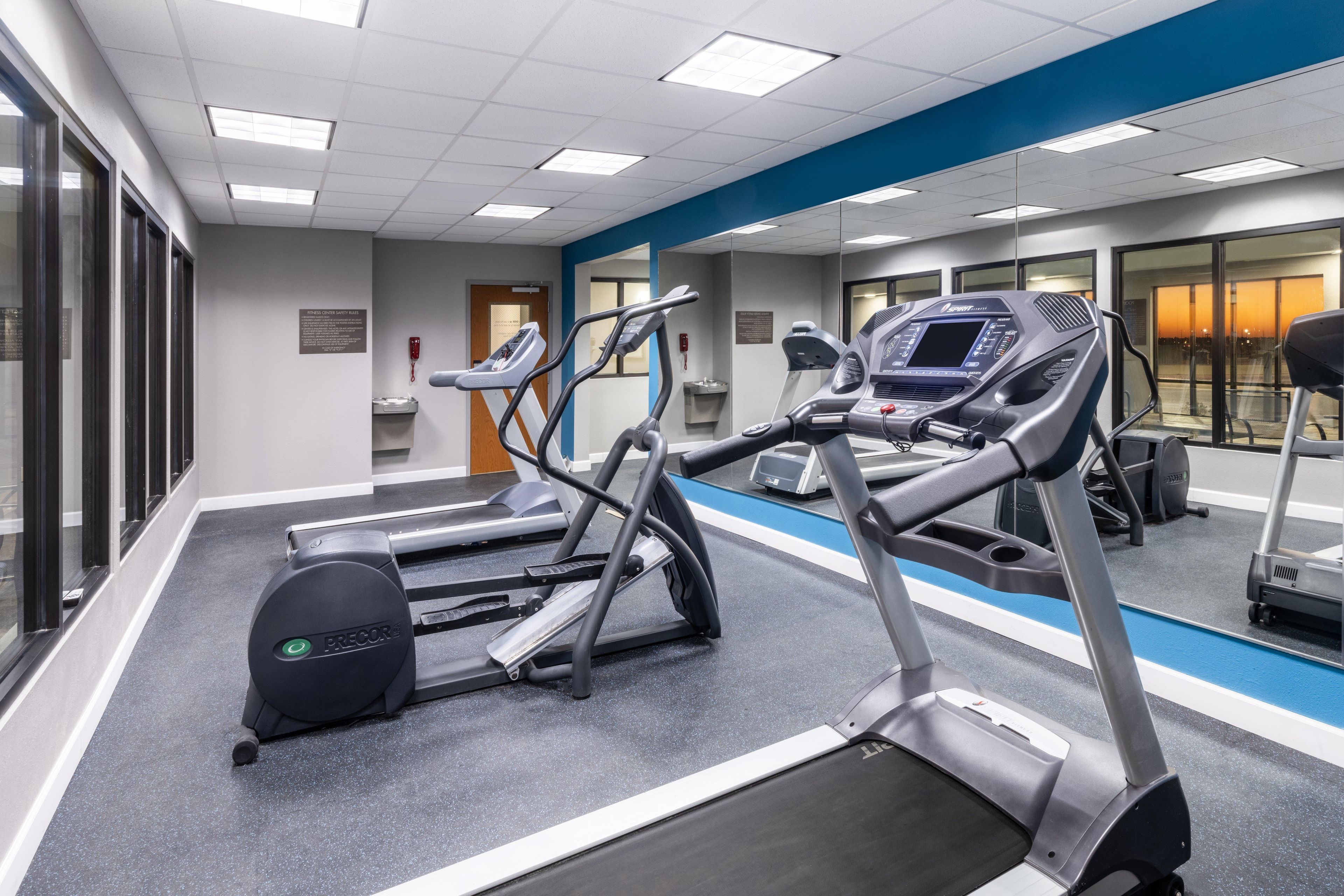 A gym with treadmills, ellipticals, and a mirrored wall.
