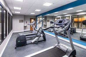Une salle de sport équipée de tapis de course, de vélos elliptiques et d’un mur recouvert de miroirs.