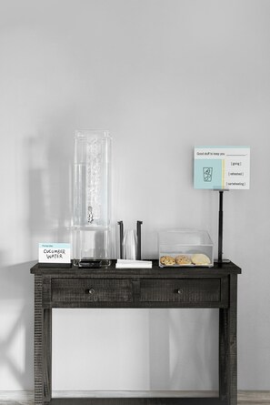 Una mesa de madera oscura con un dispensador de agua, un cartel con un dibujo y un recipiente con galletas.