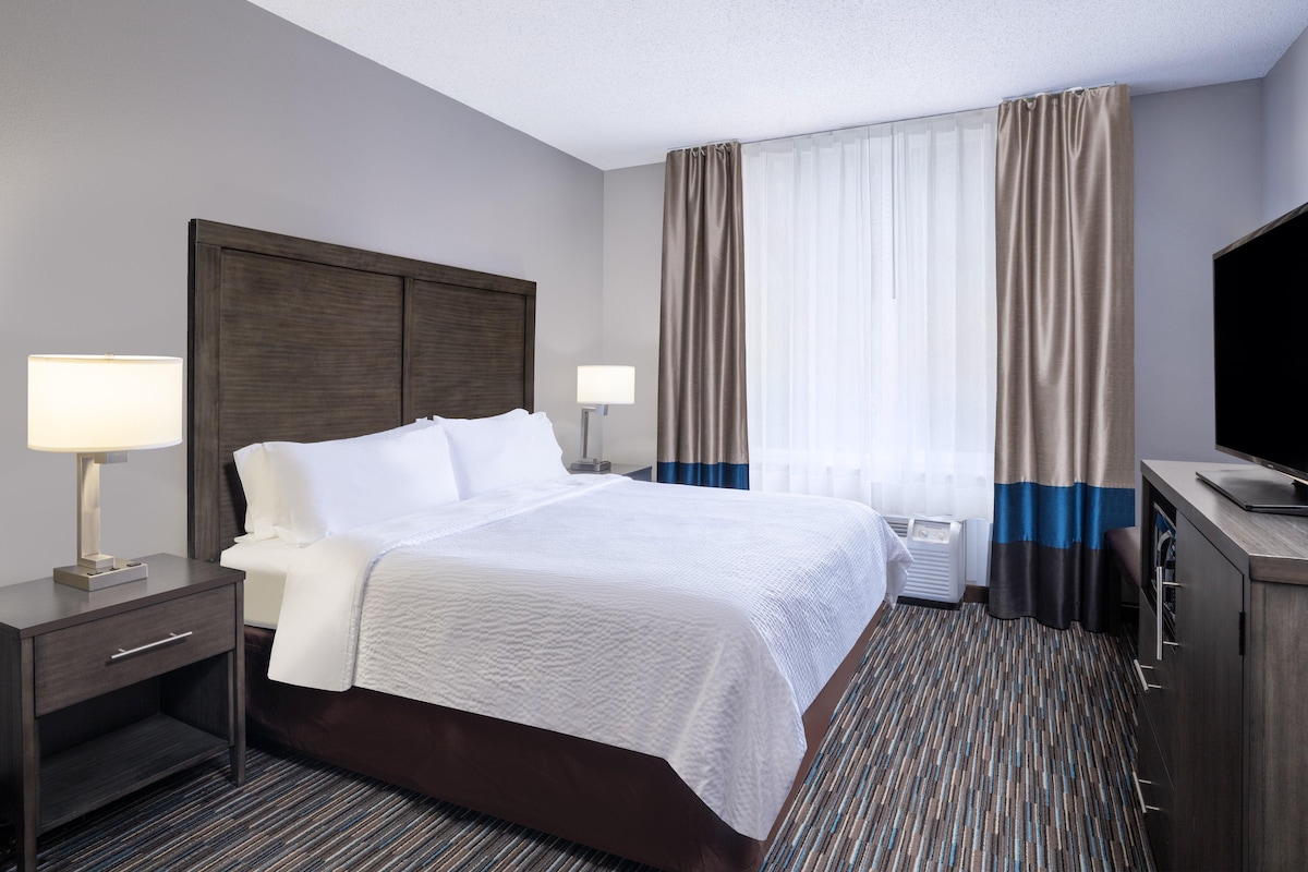 A hotel room with a large bed, bedside tables with lamps, a flat-screen TV, and a window with curtains.