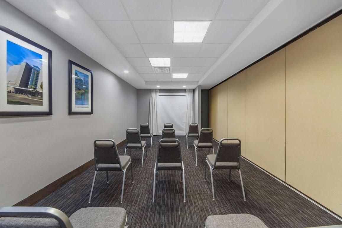 A conference room with rows of chairs, a white curtain, framed pictures on the wall, and a carpeted floor.