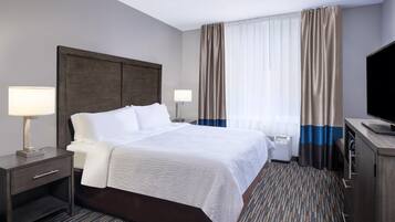 A hotel room with a large bed, bedside tables with lamps, a flat-screen TV, and a window with curtains.