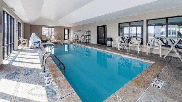 An indoor swimming pool with clear water, surrounded by chairs and tables, and large windows on one side.