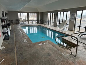 Una piscina interior con paredes de vidrio transparente, suelo de baldosas y una silla para socorrista.