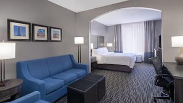 Quarto de hotel com sofá azul, cama, escrivaninha com cadeira e quadros nas paredes.