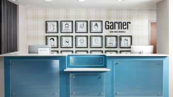 A hotel reception desk with framed artwork on the wall and a sign that reads 'Garner An High Hotel.'