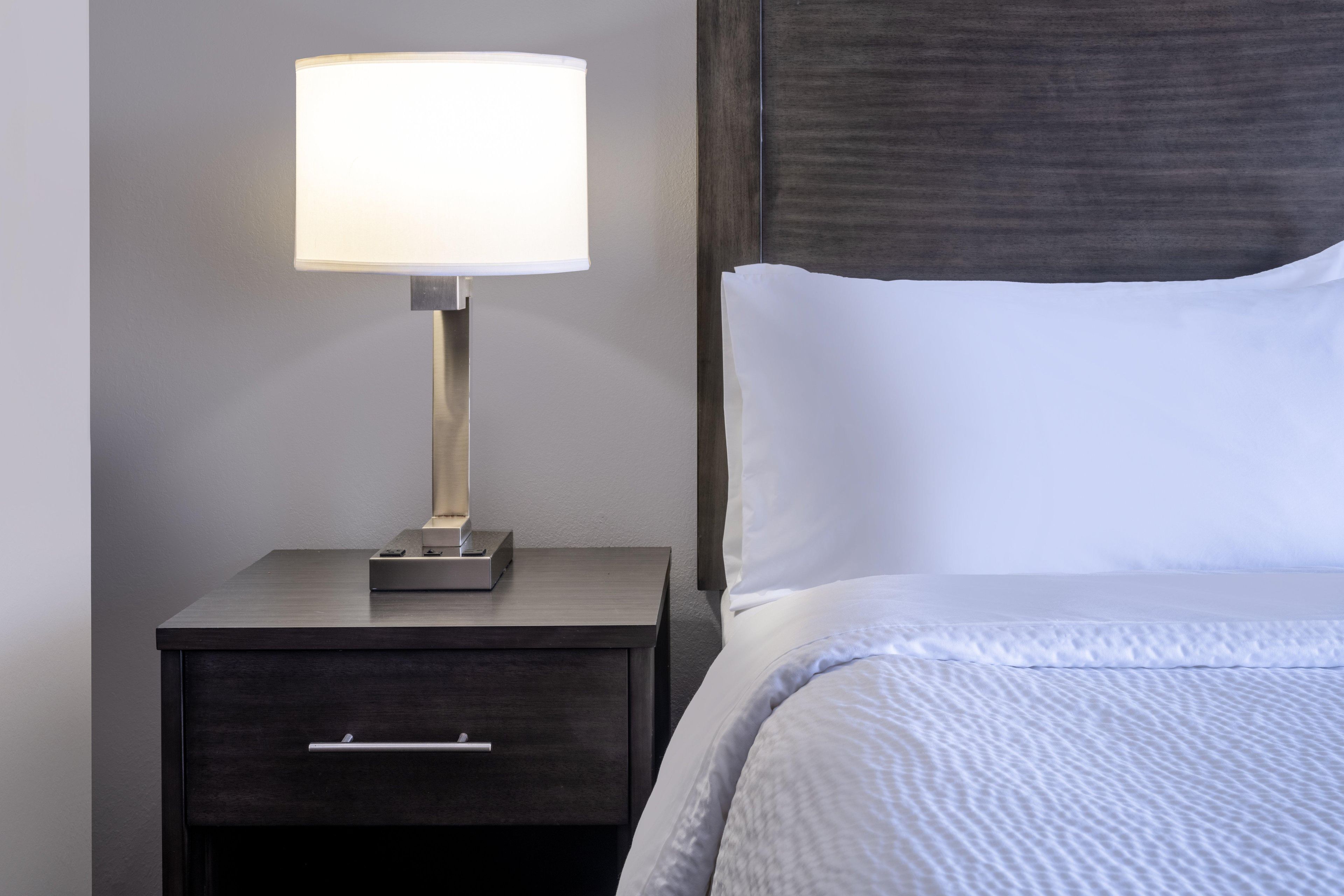 A neatly made bed with white linens and a dark wooden nightstand beside it.
