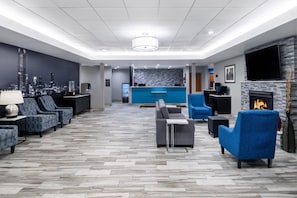 A hotel lobby with a reception desk, seating area, fireplace, and a cityscape mural. - Garner Oklahoma City Quail Springs (Oklahoma City)