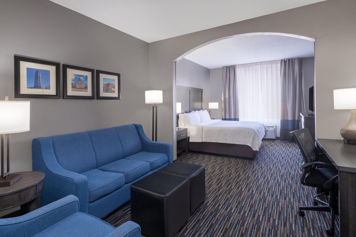 A hotel room with a blue sofa, a bed, a desk with a chair, and framed pictures on the wall.