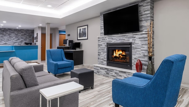Una sala de estar moderna con chimenea, sofás azules y grises, un televisor de pantalla plana y una zona de cocina al fondo.