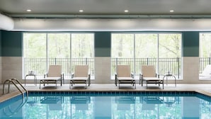 Una piscina con cuatro sillas de descanso, ventanas amplias y vistas a árboles.