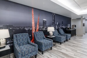 Un hall d’hôtel orné d’une fresque représentant un paysage urbain, avec quatre fauteuils à motifs, un appareil à café et une lampe.