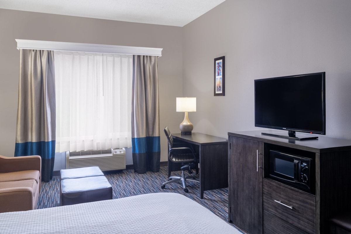 A hotel room with a bed, a desk with a computer, a television, a lamp, and a microwave.