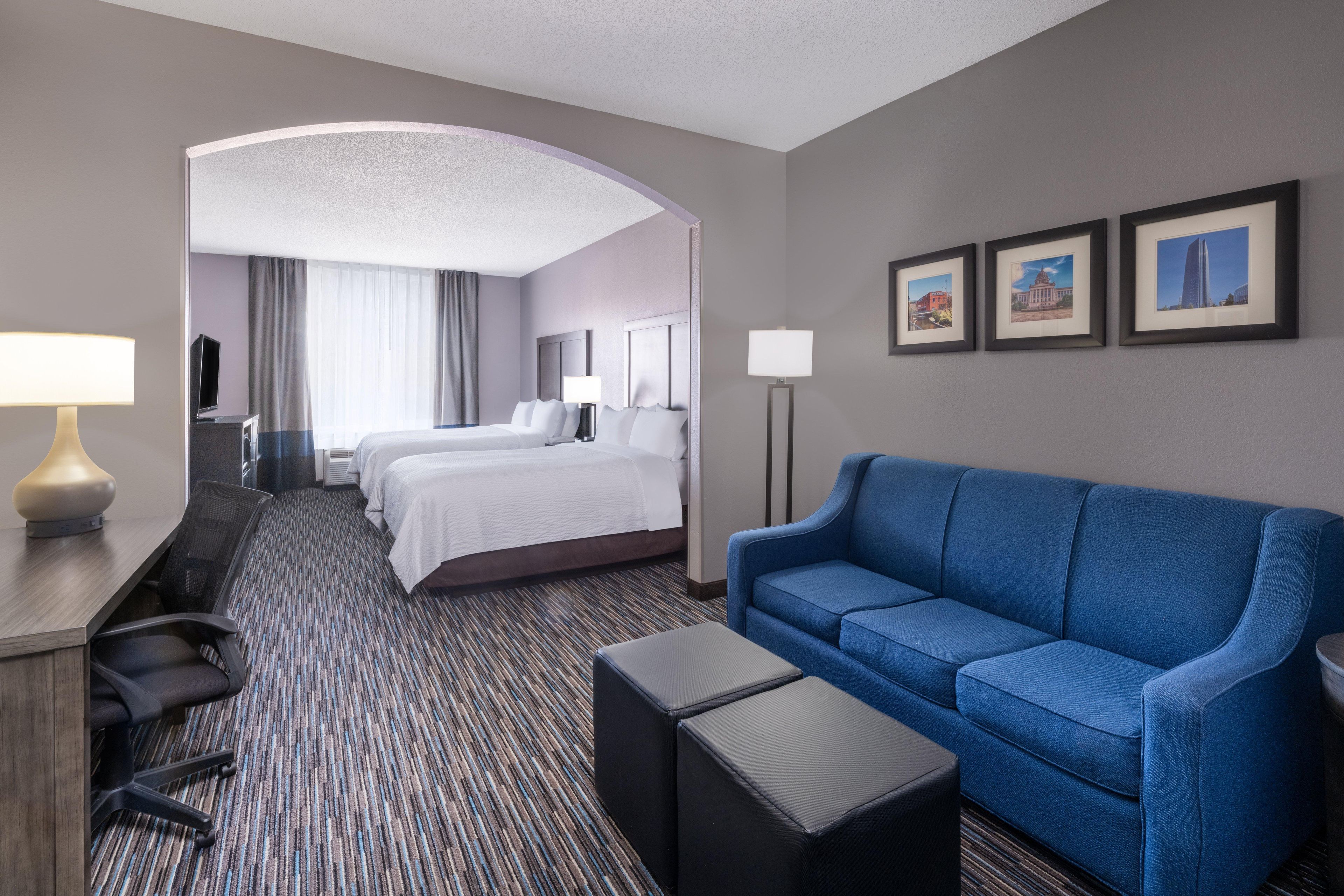 A hotel room with a large bed, a blue sofa, a desk with a lamp, and a flat-screen TV.