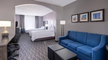 A hotel room with a large bed, a blue sofa, a desk with a lamp, and a flat-screen TV.