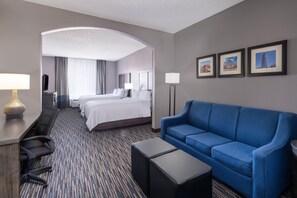 A hotel room with a large bed, a blue sofa, a desk with a lamp, and a flat-screen TV.