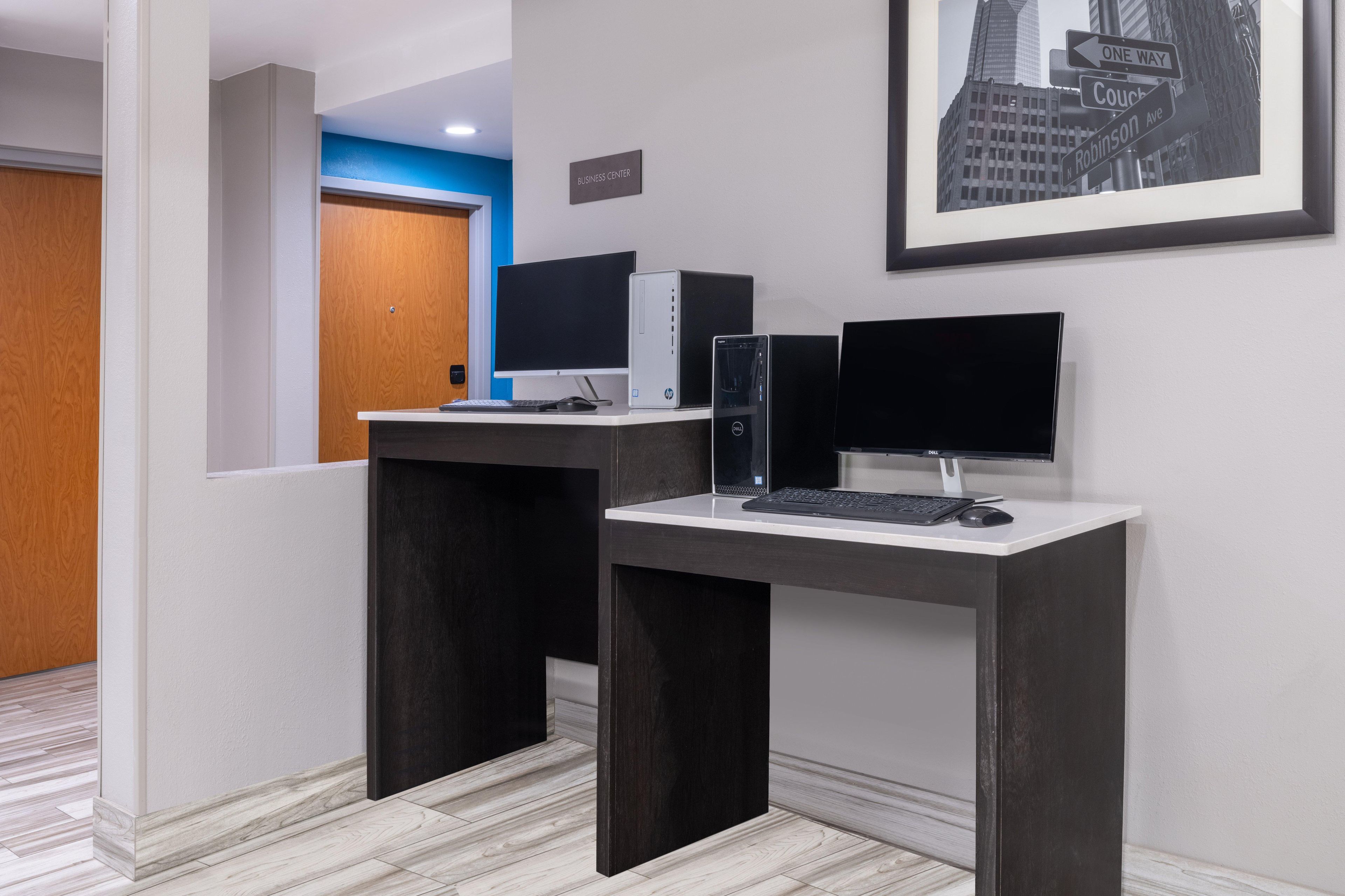 A reception desk with a computer, a framed cityscape, and a sign reading 'BUSINESS CENTER.'