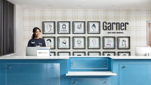 A hotel reception desk with framed artwork on the wall, a blue counter, and a nameplate reading 'IHG ONE OF A KIND.'