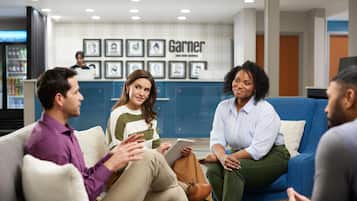Eine Gruppe von Menschen sitzt auf einer Couch in einer Lobby mit einer Rezeption und gerahmten Bildern an der Wand.