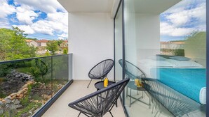 Un balcon avec deux chaises à l’assise en fil de fer noir, une table en verre et une piscine couverte par une paroi de verre.