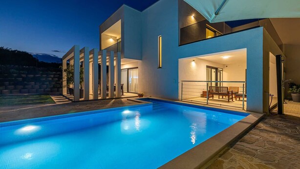 Une maison moderne dotée d’une piscine, d’un espace salon extérieur et d’un grand parasol.