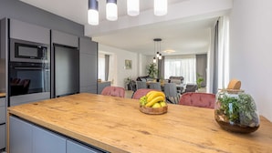 Une cuisine moderne avec un plan de travail en bois, un four à micro-ondes encastré et un réfrigérateur. On y trouve un coin repas avec une table et des chaises, ainsi qu’une plante sur le rebord de la fenêtre.