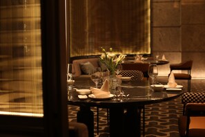 A dining table set with white napkins, plates, and glasses, surrounded by chairs and a sofa in a dimly lit room with patterned carpet. - Crowne Plaza Shangluo (Shanglou)