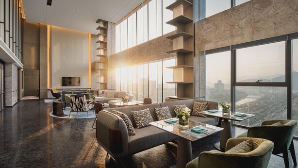 A modern hotel lobby with a high ceiling, a central seating area with sofas and chairs, a staircase, and large windows offering a city view. - Crowne Plaza Shangluo (Shanglou)