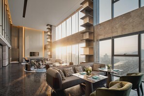 A modern hotel lobby with a high ceiling, a central seating area with sofas and chairs, a staircase, and large windows offering a city view. - Crowne Plaza Shangluo (Shanglou)